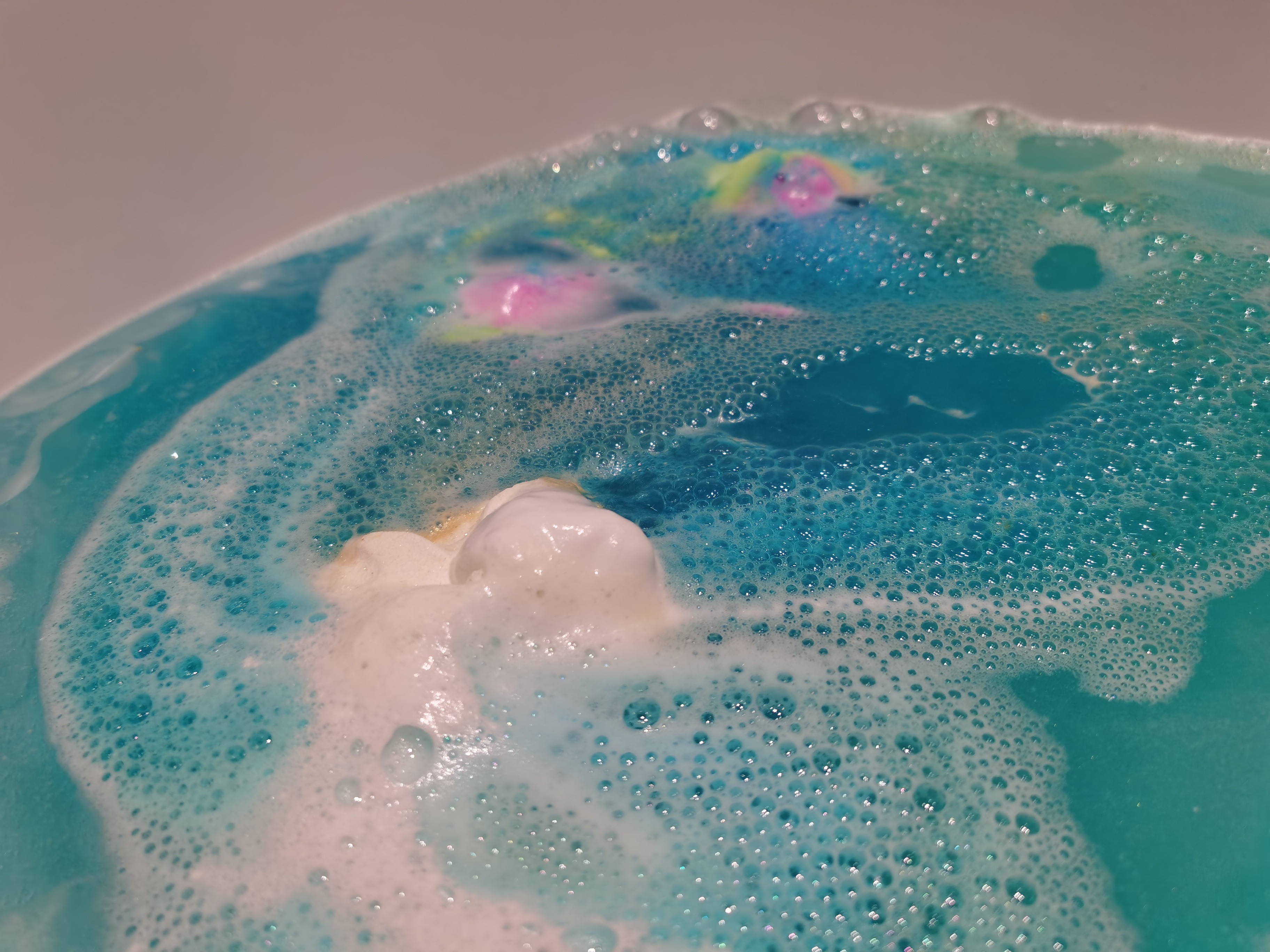 Golden Wonder Bath Bomb by Lush dissolving into blue water and releasing rainbow embeds