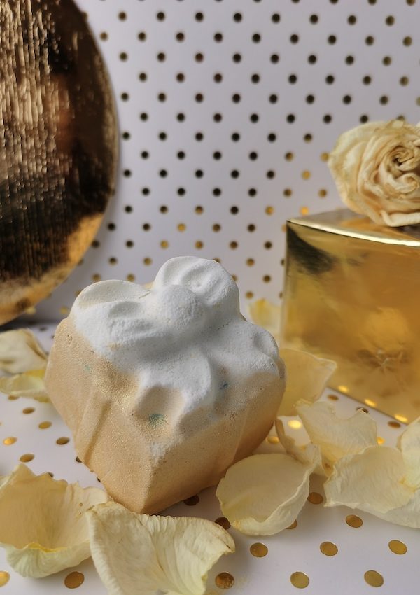 Golden Wonder Bath Bomb by Lush with white rose petals, a golden balloon and golden gift on a white and gold background