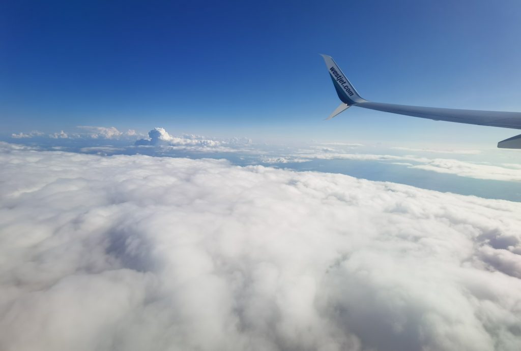 Westjet airplane wing visible over clouds