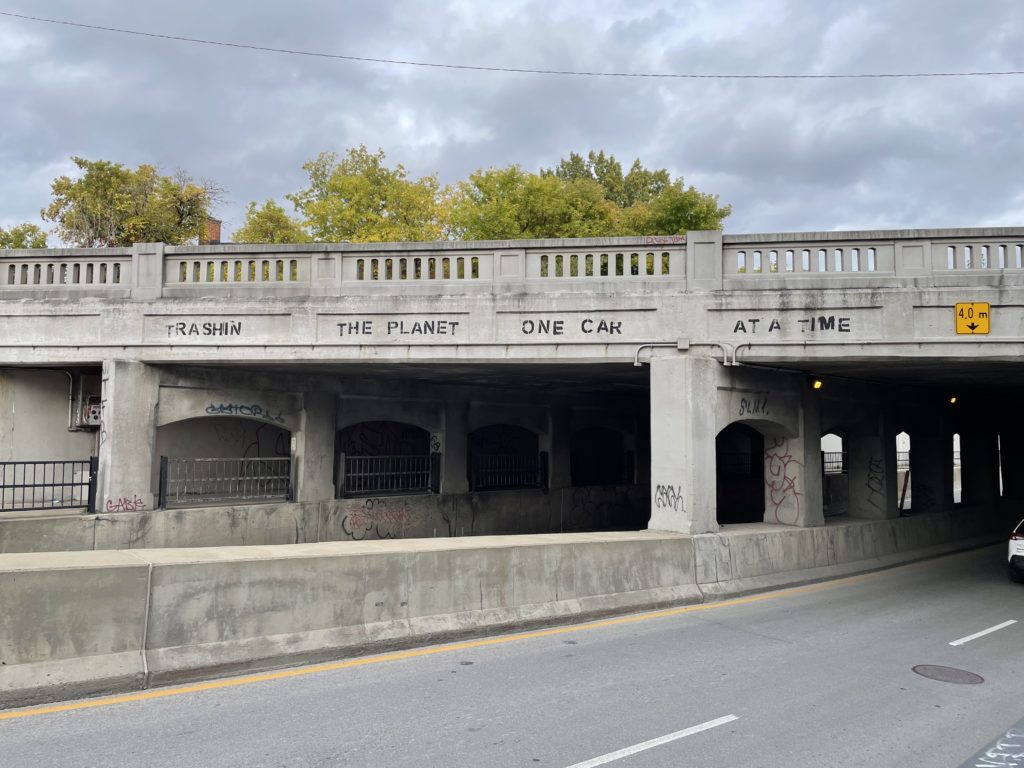 Graffiti saying “Trashin the planet one car at a time” on the side of a bridge