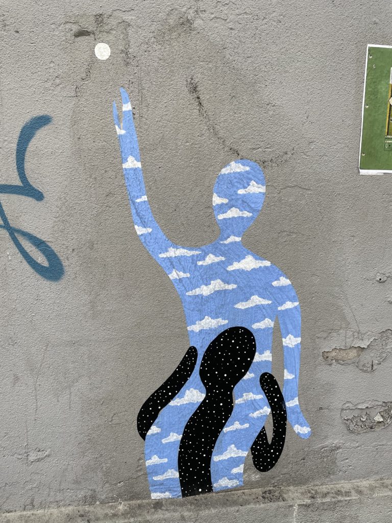 Graffiti of a blue shaped-person with cloud patterns trying to touch a small white sphere held by a black silhouette with white dots